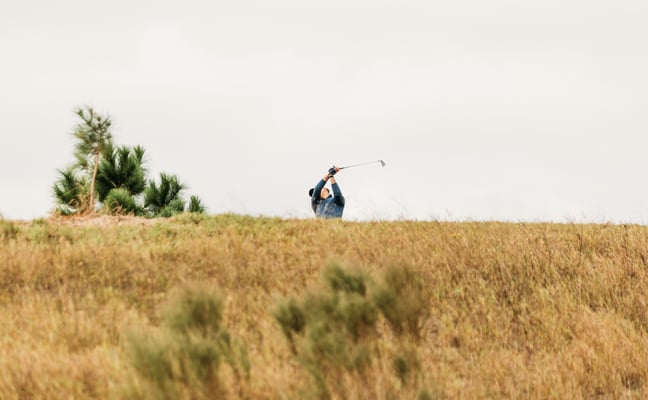 Golfer swinging on a hill with pine trees